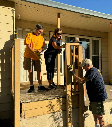 A group of people working together to build or repair a wooden porch.